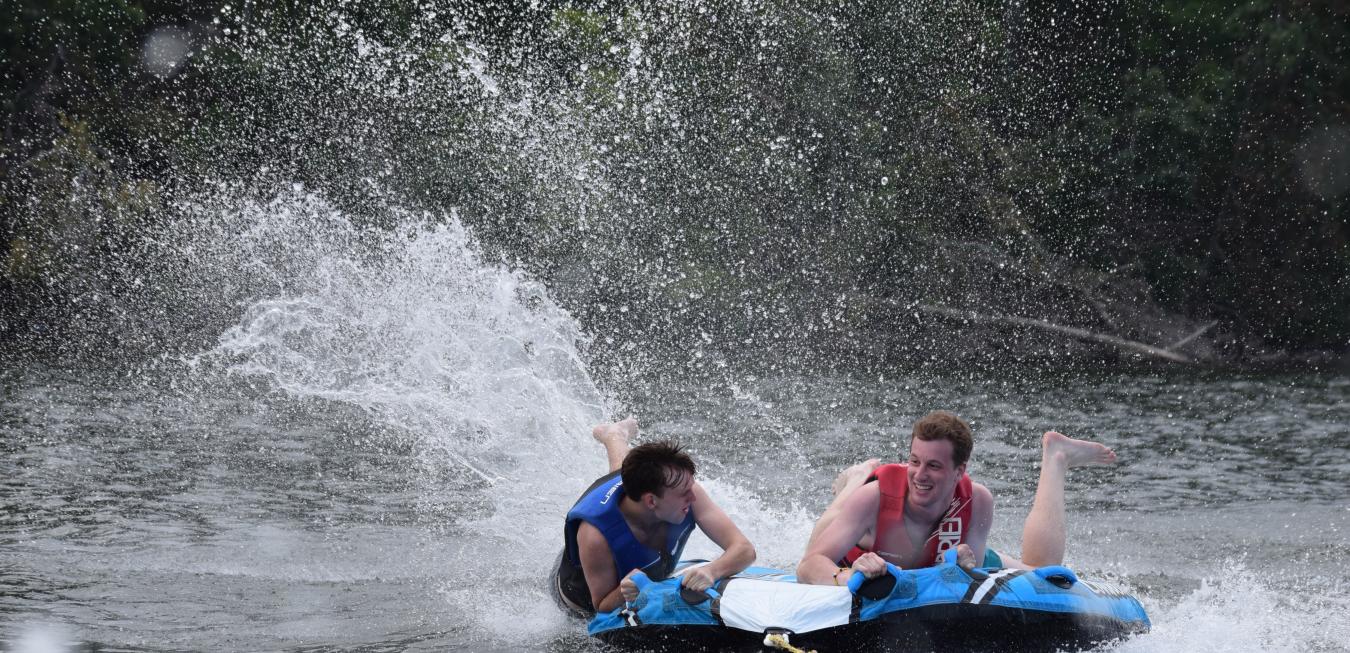 Image: Two camp Trulaske students on an inter tube being pulled on a lake.