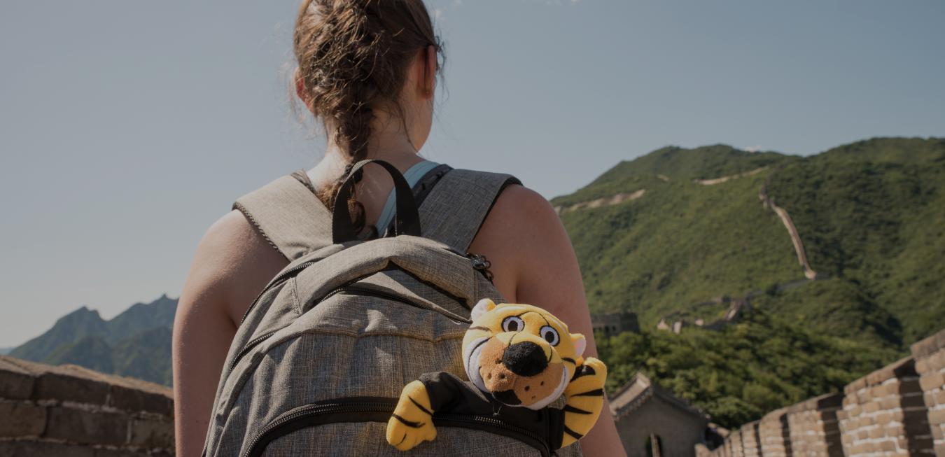 Image: Female student turned away wearing backpack on the Great Wall of China with toy Truman the Tiger sticking out.