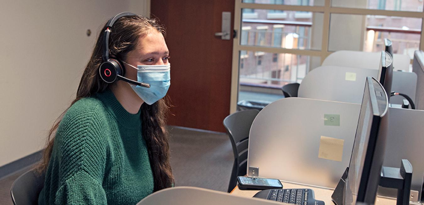 Student working at a computer in the Inside Sales lab, wearing a mask