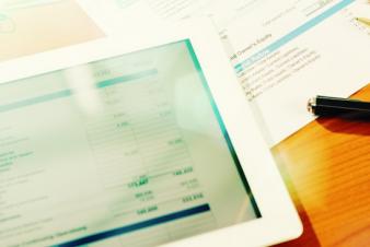 Image: Close up of a tablet computer on a desk with pens and worksheets next to it.