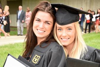Image: Two female students wearing MU graduation caps and gowns.