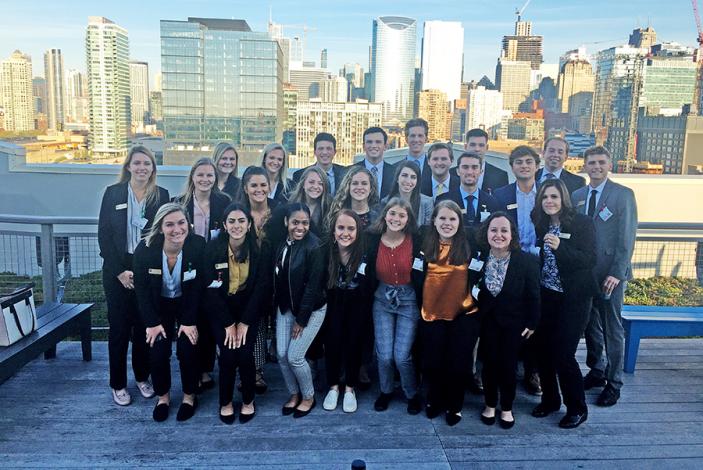 Image: A group of students standing on a rooftop with a city skyline behind them.