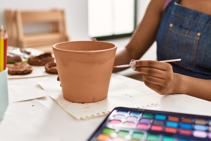 A young artist paints a flower pot.