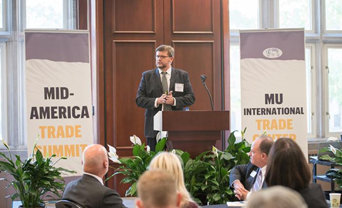 Image: A man speaking at the front of the room with a pull-up banner on each side of him.